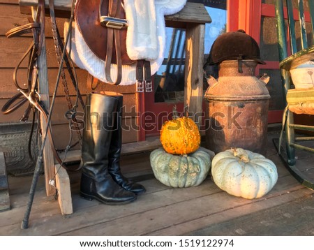 Autumn still life of a farmhouse front porch with a leather saddle riding boots bridle
Pumpkins milk jug rocking chair