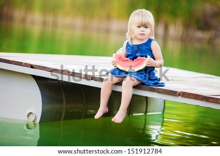 Happy smiling child eating watermelon on lake