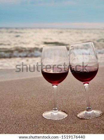 Wineglass with red wine on the beach at sunset. Romantic concept.