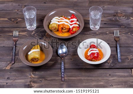 Five stuffed peppers in sour cream in three plates with two glasses of water, top view