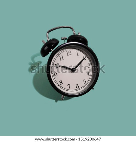Black classic style alarm clock with hard shadow isolated on green background. Smile time concept