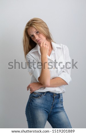 portrait of a young beautiful girl in a white shirt and jeans on a gray background