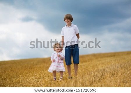 Brother and baby sister walking in a golden wheat field at sunset