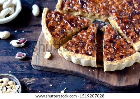 Tart with condensed milk and peanuts on a dark wooden background