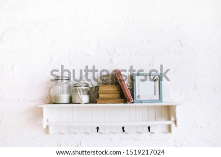 Handmade wooden shelf with books, picture frame and candles in glass bottles. Cozy rustic style, white background. Stucco molding wall.
