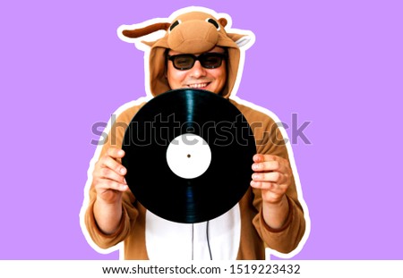 Man in cosplay costume of a cow with gramophone record isolated on purple background. Guy in the animal pyjamas sleepwear. Funny photo with party ideas. Disco retro music.