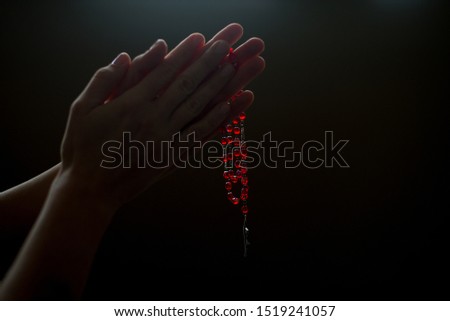 Female hands holding and hanging a red rosary on black background. Woman with Christian Catholic religious faith. Closeup image of hands and rosary. Holding rosary with white background