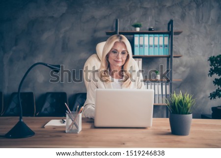 Photo of old white haired woman working with her laptop online with her coworkers using modern technology to communicate with corporation team