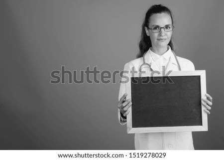 Young beautiful woman doctor holding empty black board with copy space