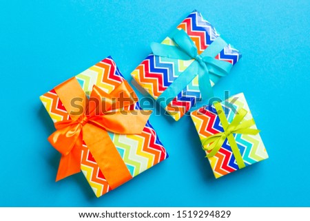 wrapped Christmas or other holiday handmade present in paper with blue, green and orange ribbon on blue background. Present box, decoration of gift on colored table, top view.