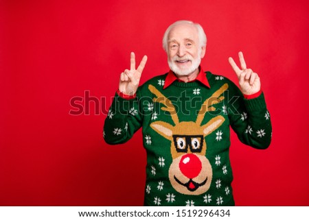 Portrait of positive cheerful grey hair old man enjoy theme noel x-mas time party make v-signs wear reindeer pattern design tradition clothes isolated over red color background