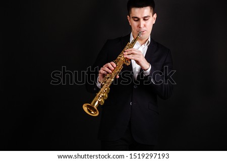Musician in a black suit on a black background playing a gold soprano Saxophone Royalty-Free Stock Photo #1519297193
