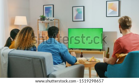 Happy Friends Sitting At Home Watching Green Chroma Key Screen, Relaxing on a Couch. Watching Sports Match, News, Sitcom TV Show or a Movie.