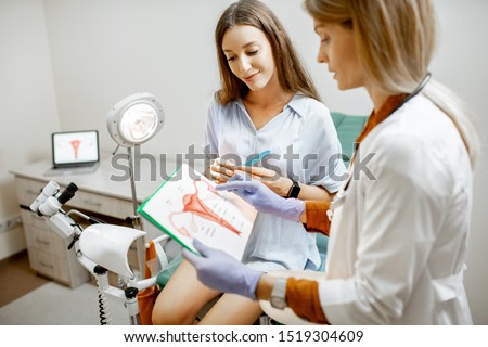 Gynecologist showing a picture with uterus to a young woman patient, explaining the features of women's health during a medical consultation in the office Royalty-Free Stock Photo #1519304609