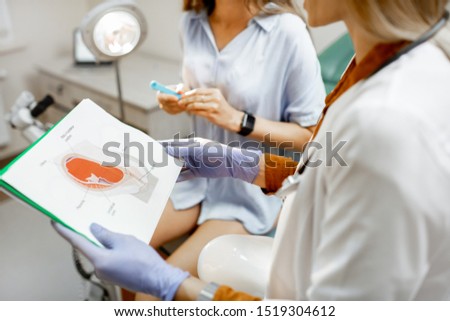 Gynecologist showing a picture with uterus to a young woman patient, explaining the features of women's health during a medical consultation in the office