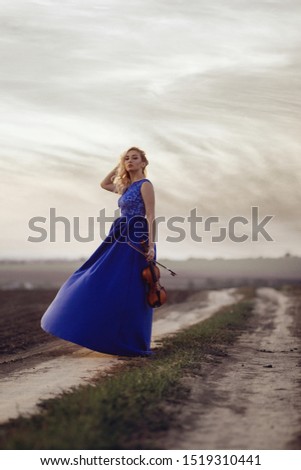 figure of young woman in long dress with violin in field at sunset, girl engaged in musical art, performance on nature, concept passion in music
