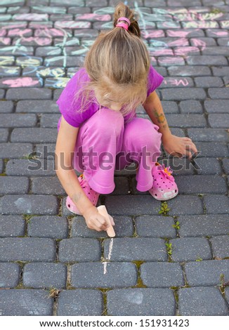 Young blond five years old caucasian girl drawing a picture outdoor on the pavement with chalk