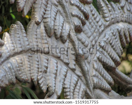 Close-up of fern pattern on antique cast iron bench with park greenery in background.