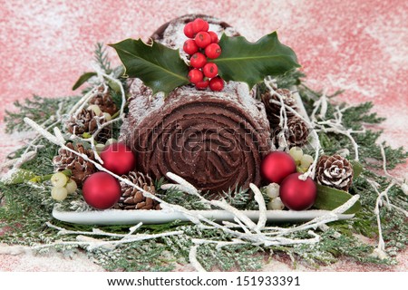 Christmas chocolate yule log cake with red bauble decorations, holly, mistletoe, snow, pine cones and winter greenery. 