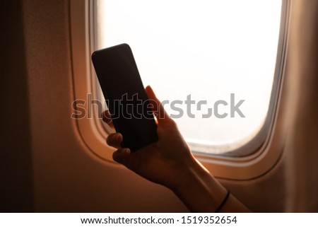 Female hand holding the smartphone on background of airplane window.