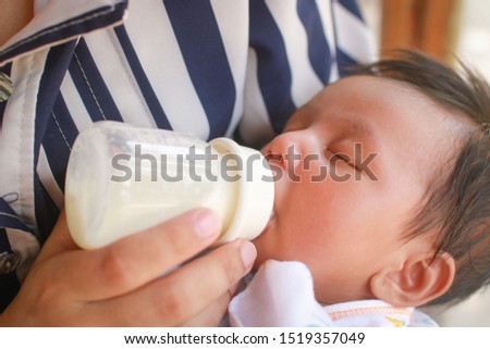 Asian baby lying on mothers hand drinking milk from bottle.