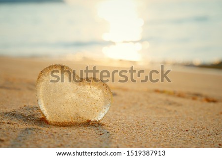 A heart shaped glass rests on a sandy beach with the reflection of the evening sun.
