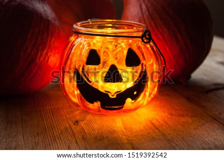 Halloween decoration concept. Scary jack-o-lantern candle holder with pumpkins on old wooden background. Selective soft focus. Shallow depth of field. Text copy space.