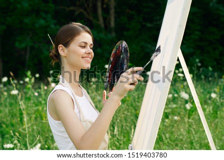 young woman with paints in a forest paints a picture