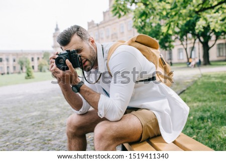 bearded man sitting on bench and taking photo 