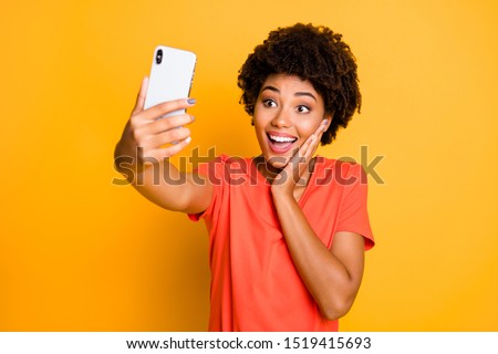 Photo of cheerful cute charming nice beautiful attractive girlfriend black skinned taking selfie with her telephone held in her hands wearing t-shirt isolated over yellow vivid color background