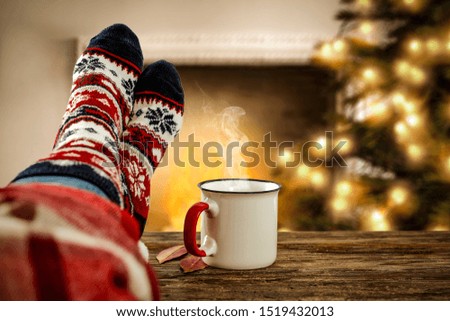 Christmas background of fireplace with xmas tree. Woman legs with wool socks and free space for your decoration. 
