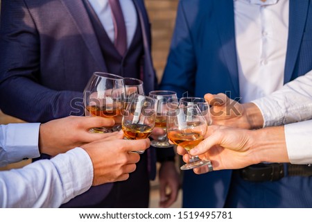 Young guys holding glasses of whiskey on holiday . Hands with glasses closeup. Royalty-Free Stock Photo #1519495781