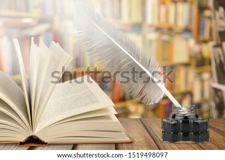 Old quill pen, books and vintage inkwell on wooden desk in the old office against the background of the bookcase and the rays of light. Conceptual background on history, education, literature topics.
