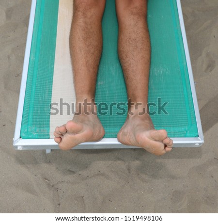 Two feet and two legs on the deck chair on the beach