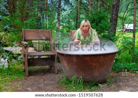 A young beautiful girl, a blonde witch is preparing a potion in a large cauldron on the eve of Halloween or the worshiping devil bringing in priesthood. Feminine witchcraft and influence on men.