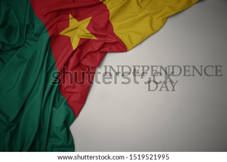 waving colorful national flag of cameroon on a gray background with text independence day. concept