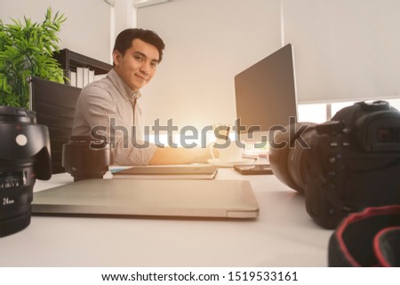 Portrait of young photographer and graphic designer sitting at graphic studio in front of laptop and computer while working.