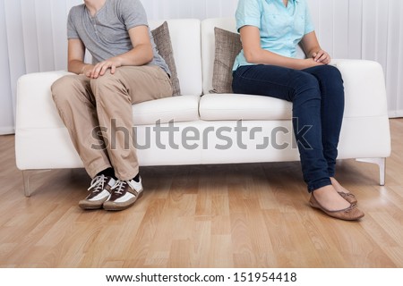 Brother and sister have had an argument and are sitting at opposite ends of a sofa Royalty-Free Stock Photo #151954418