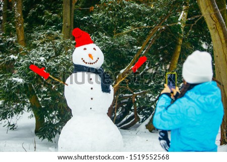 woman taking picture of snowman on phone