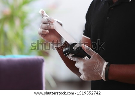 Waiter's hands in gloves with a terminal. The concept of customer service in a restaurant. African American waiter. Check in the terminal. Payment by bank card, bank transfer.  Photo without a face.