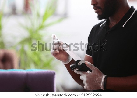 Waiter's hands in gloves with a terminal. The concept of customer service in a restaurant. African American waiter. Payment by bank card, bank transfer. Photo in the interior. Photo without a face.