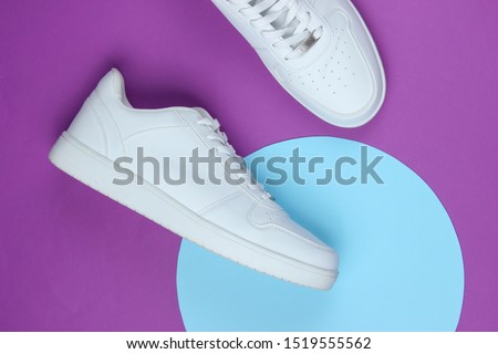 White sneakers on purple background with blue pastel circle. Youth hipster concept. Top view