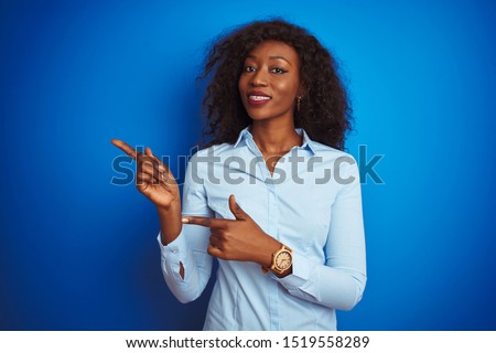 African american businesswoman wearing shirt standing over isolated blue background smiling and looking at the camera pointing with two hands and fingers to the side.