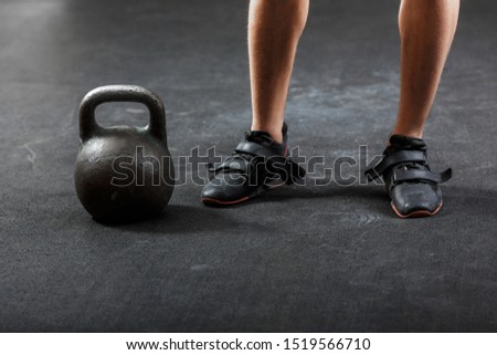 A man's feet in black sporting sneakers with black gymnastic kettlebell, standing near right foot