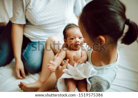Asian girl child holds sibling newborn for the first time. Childhood memory. Mother teaches daughter how to hold a baby in white napkin. Family bonding and happiness. Sisterly love. 