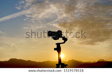 Sunset silhouette of professional dslr camera on stabilizer rig.