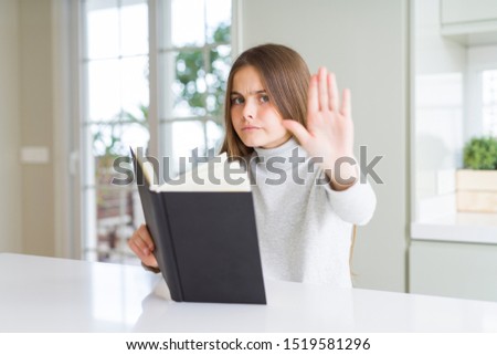 Beautiful young girl reading a book at home with open hand doing stop sign with serious and confident expression, defense gesture