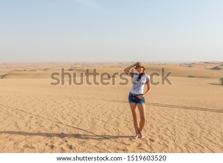 Happy attractive smiling woman wearing straw hat posing in desert sand. Travel safari on vacation, sunny summer day. United Arab Emirates