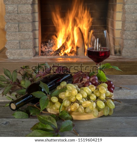 A glass of wine and a bottle of wine, fresh grapes on a table, near cozy fireplace, in country house, winter vacation, christmas.