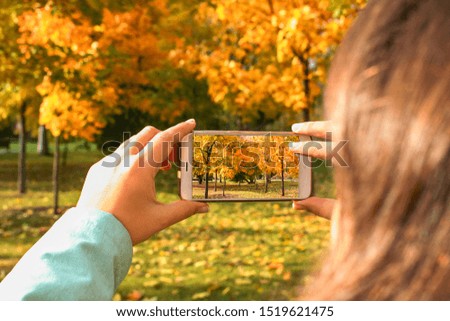 The girl takes a photo of autumn trees on the smart phone.